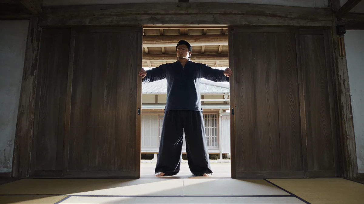 木造の道場で大きな扉を開く人物を正面から捉えた実写的な映像表現サンプル